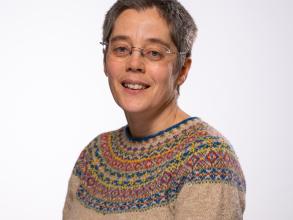 A white woman with short dark hair smiles at the camera. She is wearing a Fair Isle jumper.